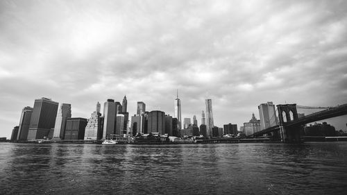 Brooklyn bridge over east river by city skyline against sky