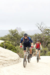 Smiling couple riding bicycles on rocks against clear sky