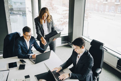 Female professional discussing with coworker over laptop while businessman working at conference table in office