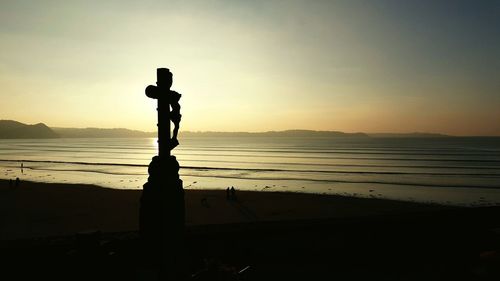 Silhouette man standing on beach against sky during sunset