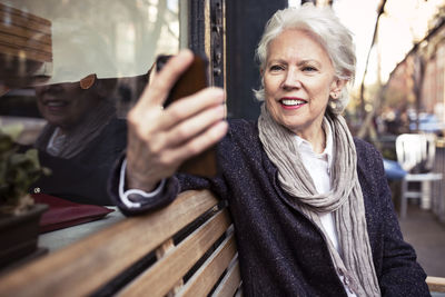 Smiling senior woman using smart phone while sitting on bench