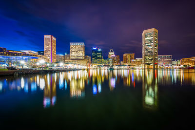 Illuminated buildings by river against sky at night