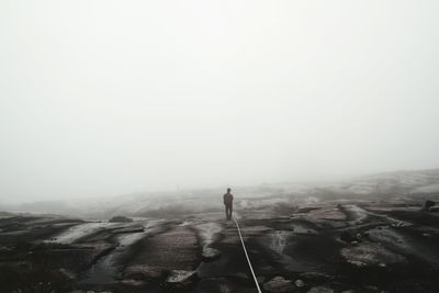 Rear view of man standing on landscape in foggy weather