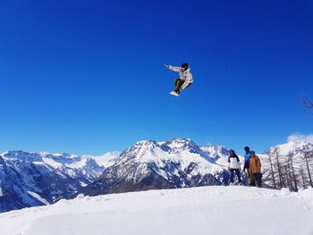 People jumping on snowcapped mountain against clear sky