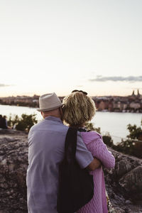 Senior man embracing woman while standing on rock at lakeshore