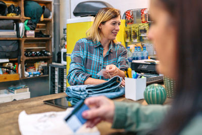 Woman employee checking on computer price of jeans and customer holding credit card to pay purchase