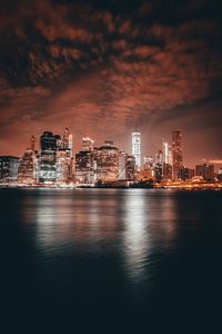 Illuminated city at waterfront during sunset