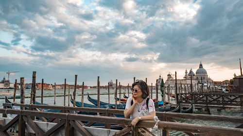 Rear view of woman sitting on bridge against cloudy sky