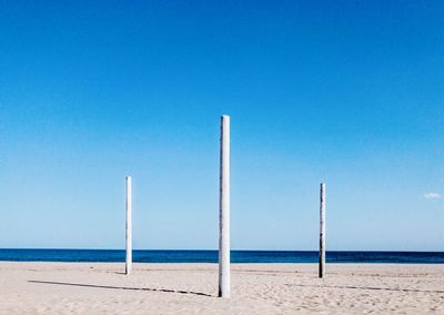 Wooden posts on beach against clear blue sky