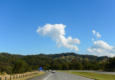 Country road by trees against blue sky