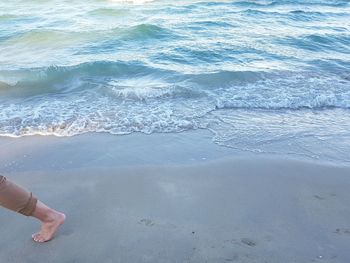 Low section of man walking on shore at beach