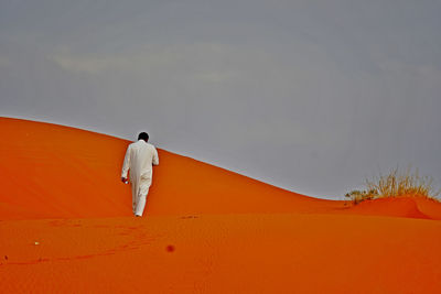 Rear view of man walking on sand dune