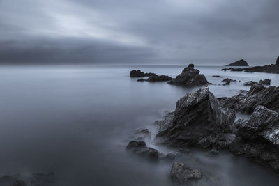 Scenic view of sea by rock formations against cloudy sky