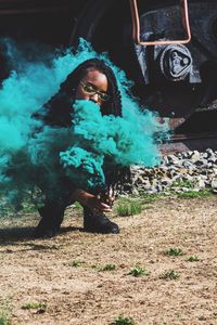 Young woman holding distress flare while crouching on field