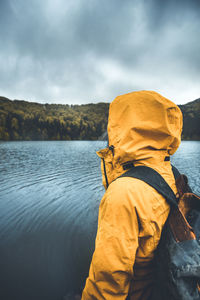 Man in hood looking at lake against sky