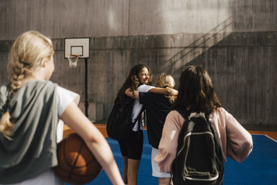 Happy female friends walking with arms around in sports court