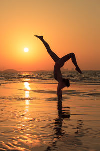 Full length of woman practicing handstand at beach during sunset