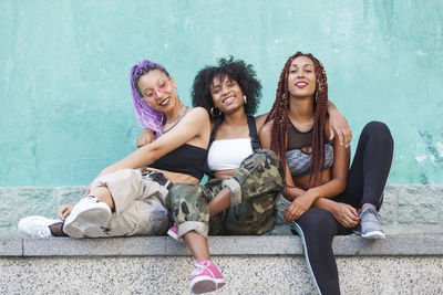 Smiling female friends sitting on retaining wall