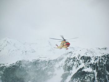 Helicopter flying against snowcapped mountains in foggy weather