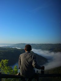 Rear view of man looking at mountains against clear sky