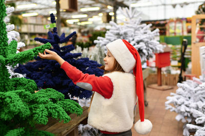 A girl and a christmas artificial trees for sale at a shop