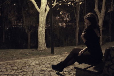 Full length of young woman sitting on bench at park during night