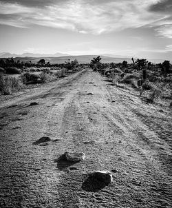 Dirt road on field against sky