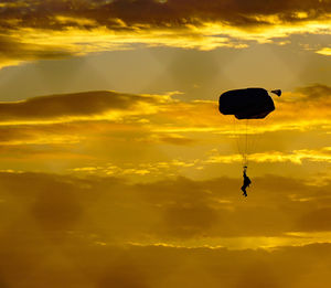 Low angle view of person paragliding against sky during sunset