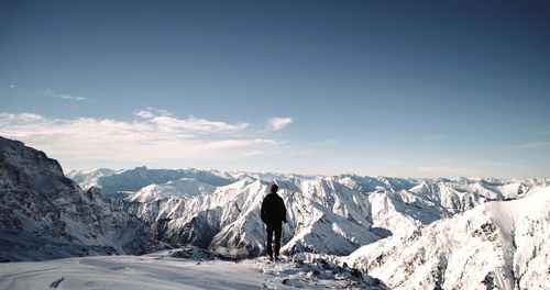 Rear view of man standing on snowcapped mountain against sky during winter