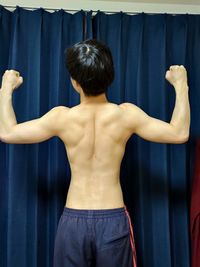 Rear view of shirtless man standing against curtain