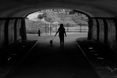 Rear view of a woman walking with dog in tunnel