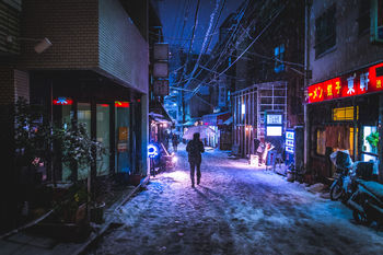 Rear view of person walking on illuminated street in city at night