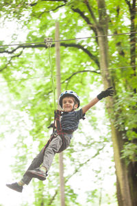 Smiling boy hanging on rope against trees