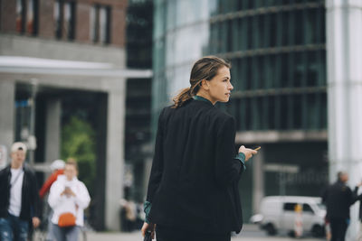 Rear view of businesswoman looking away while walking on street in city