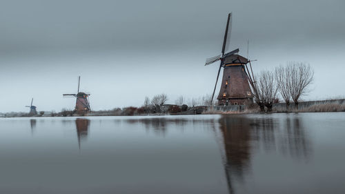 Traditional windmill by lake against dark sky