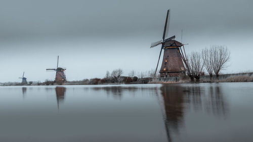 Traditional windmill by lake against sky