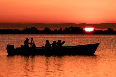Silhouette people on boat in lake against orange sky