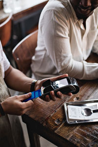 Cropped image of owner using credit card reader by customers at table in restaurant