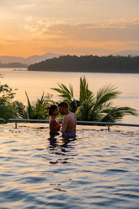 People in swimming pool against sky during sunset