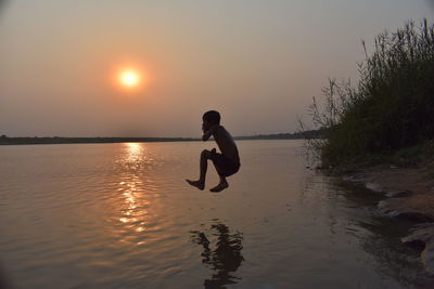 Full length of boy jumping over lake against sky during sunset