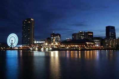 Illuminated buildings by river against sky at night