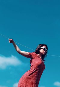 Young woman with arms raised standing against blue sky