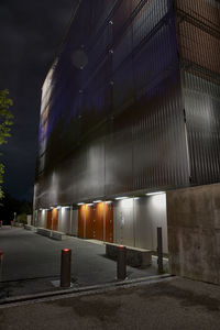 Empty road by illuminated building at night