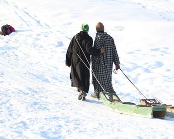 Rear view of people on pulling sled on snow covered field