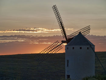 Traditional windmill on landscape against sky during sunset