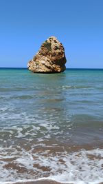 Rock formation in sea against clear blue sky