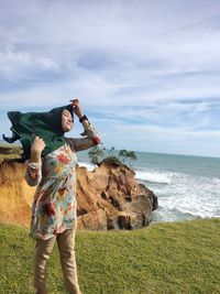 Man standing on rock by sea against sky