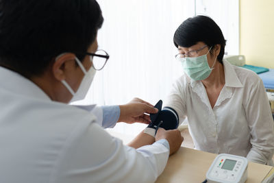 Rear view of doctor wearing mask checking blood pressure at hospital