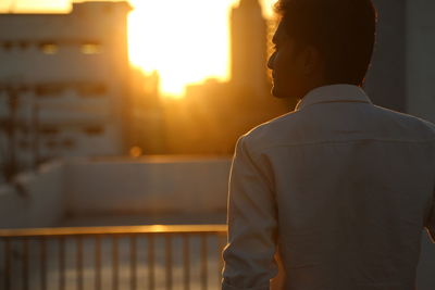Rear view of man standing against railing during sunset