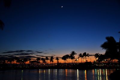 Silhouette palm trees by swimming pool against sky at sunset